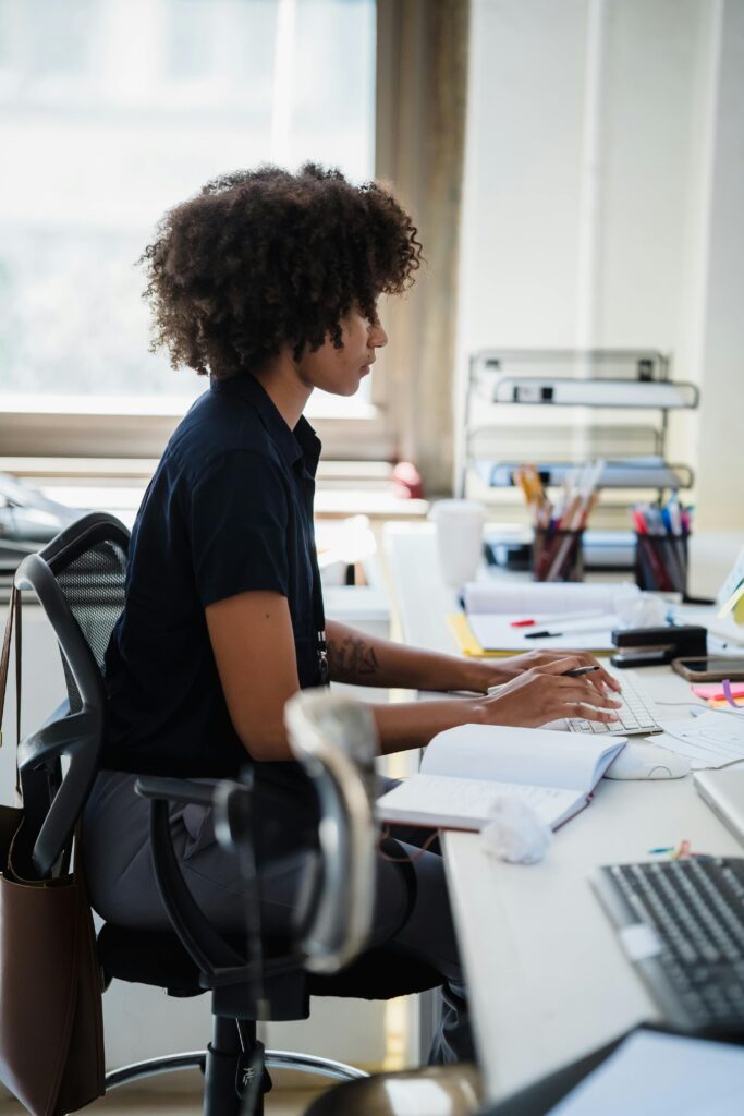 Side view of a professional woman focused on typing at a desk in a modern office setting.