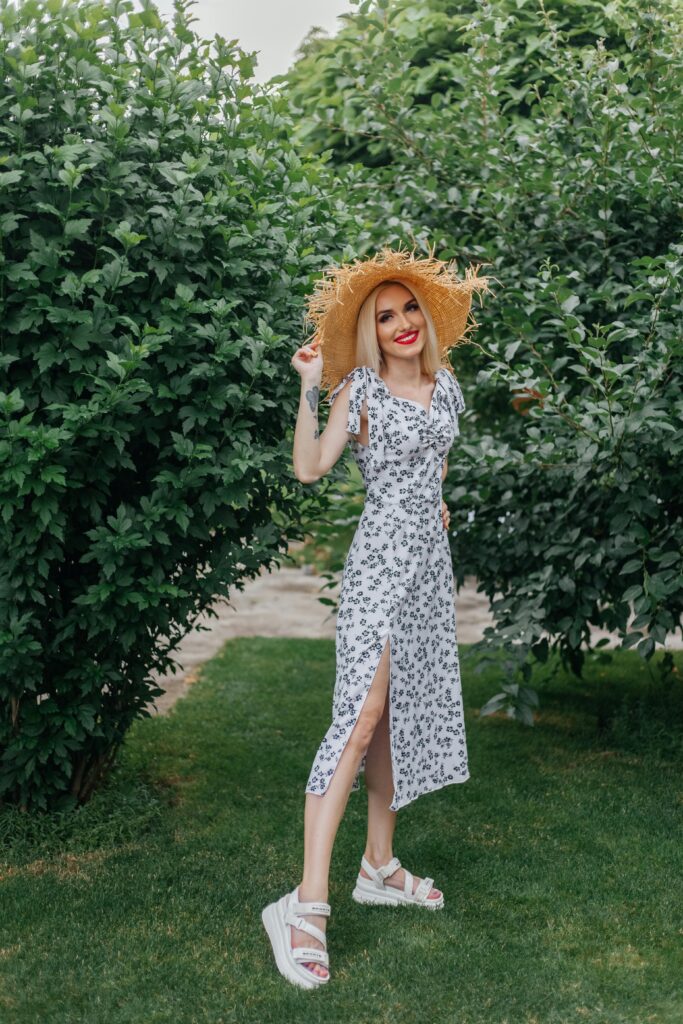 Elegant woman in a floral sundress and straw hat enjoying a summer day outdoors.