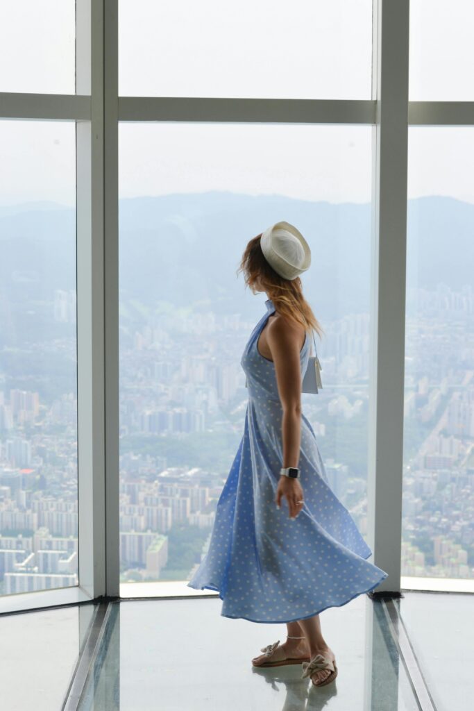 A stylish woman in a blue dress poses in a tower overlooking Seoul, offering a breathtaking city view.