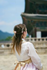 A woman in a traditional hanbok admires the architecture of a Korean palace during summer.