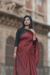 Woman wearing a red saree stands in front of historic architecture, exuding elegance and cultural beauty.