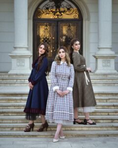Three women in vintage dresses pose gracefully on manor steps. Beautiful and elegant fashion portrait.