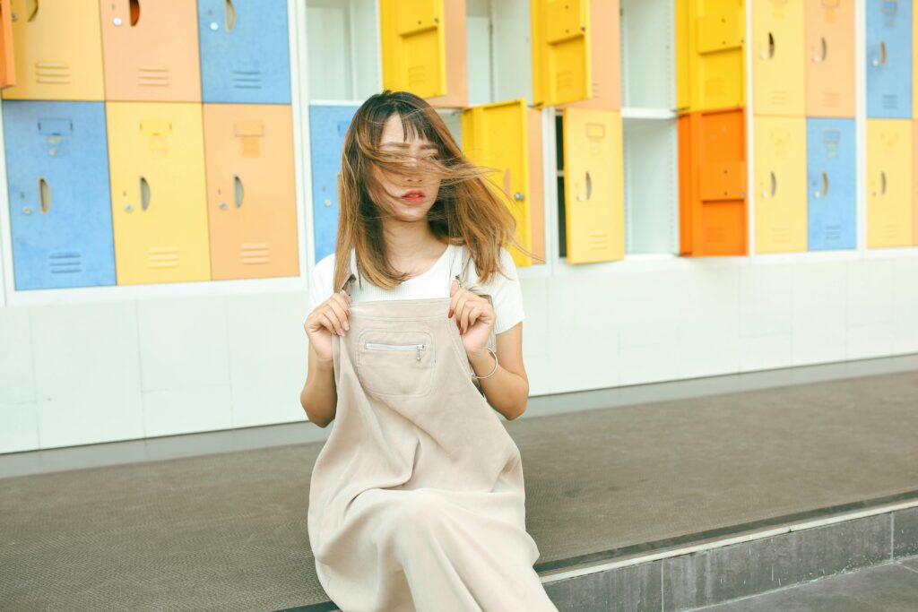 Trendy young woman sitting in front of vibrant lockers with her hair blowing in the wind.