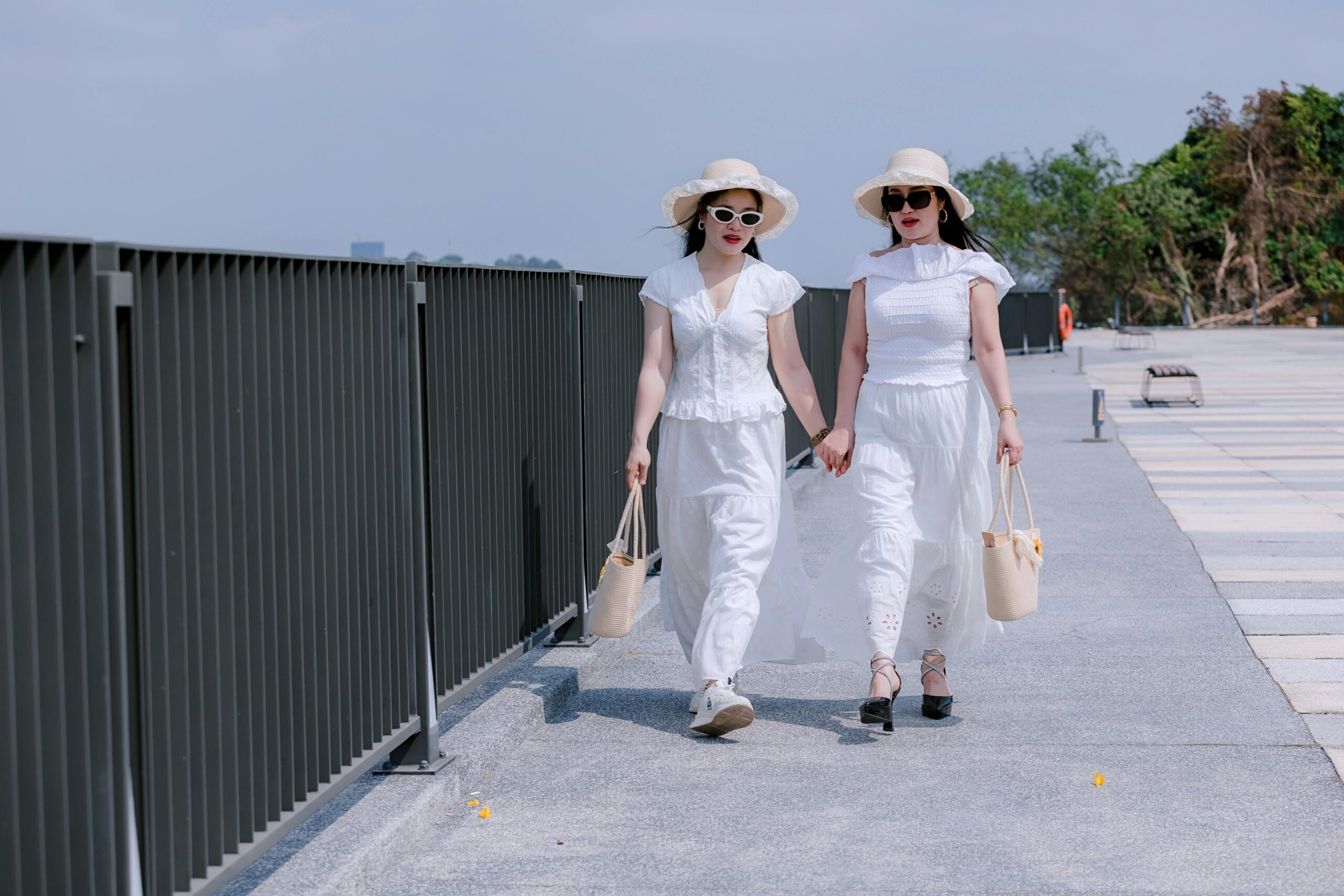 Two women in white summer outfits walking hand in hand outdoors.