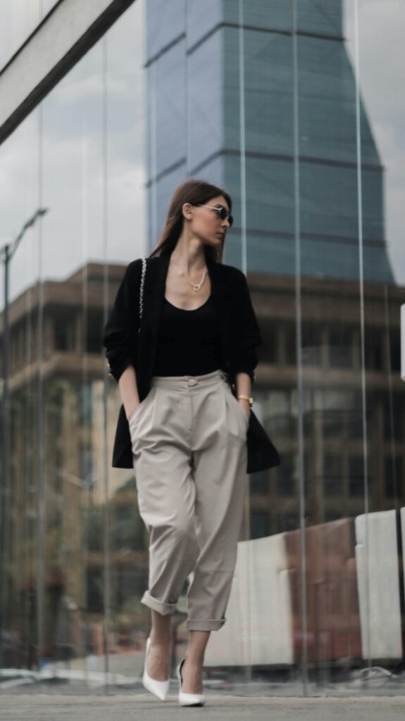 Low angle full body of confident female with hands in pockets wearing trendy clothes walking near contemporary glass facades