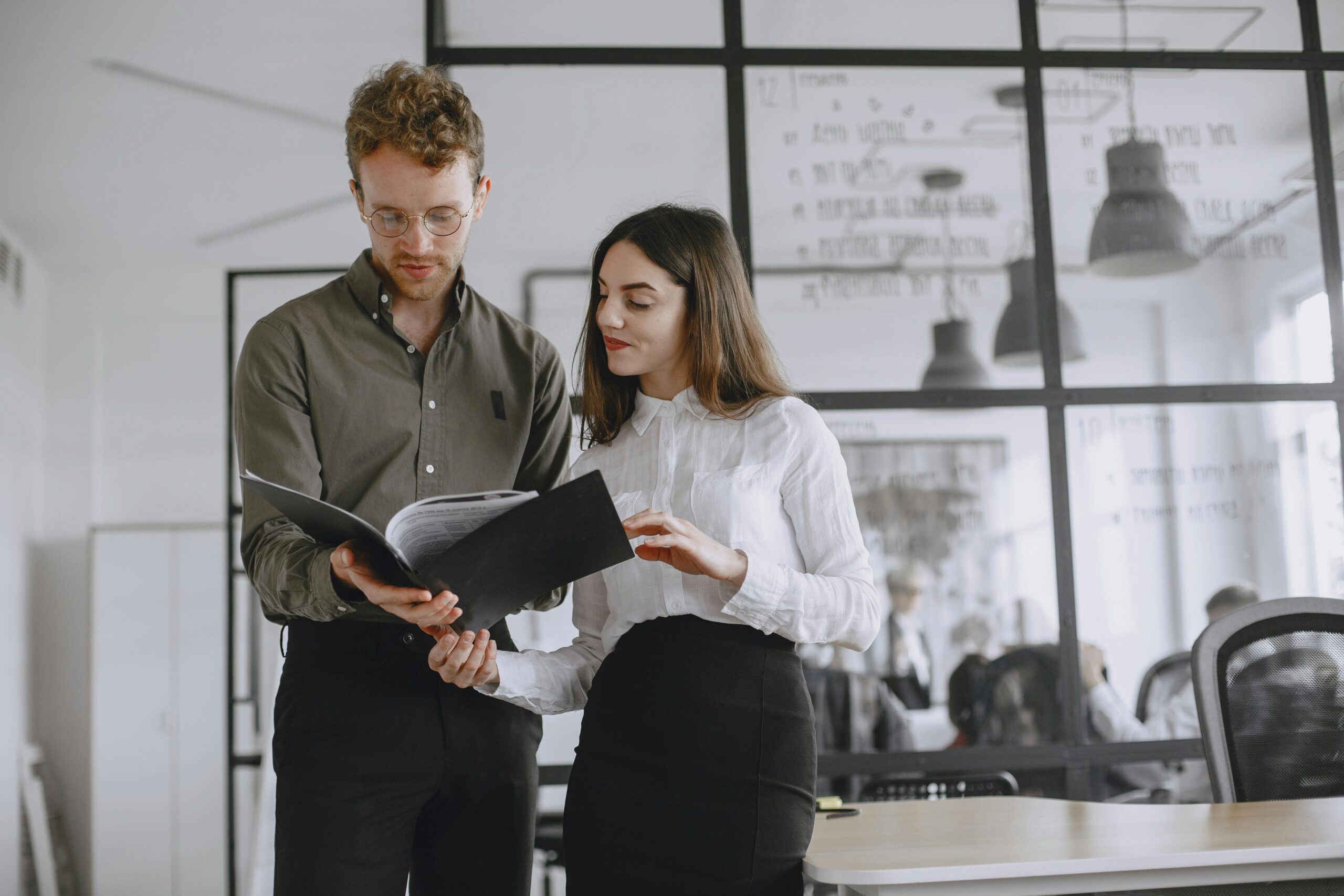 Two professionals discuss documents in a modern office environment.