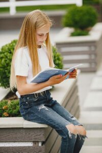 Young girl reading a book outdoors, enjoying a sunny day. Perfect for education and lifestyle concepts.